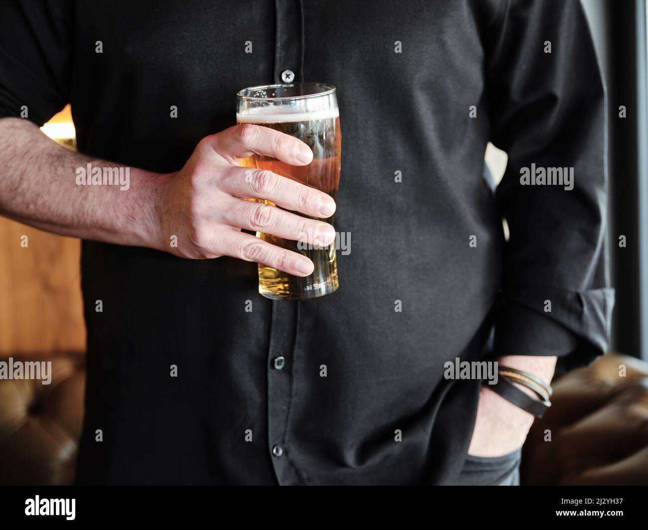 Mani di un uomo che tiene un bicchiere di birra al bar o al pub. Foto Stock