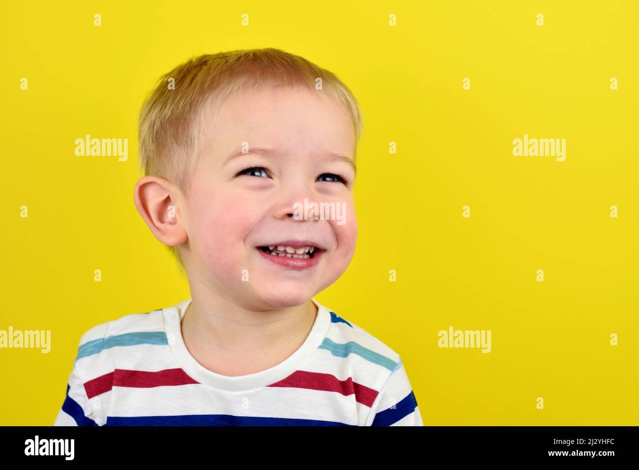 Primo piano Ritratto di un bel ragazzo ridendo. Adorabile bambino piccolo ride su sfondo giallo. Carino ragazzo sorridente e ridente. Ricerca in alto Foto Stock