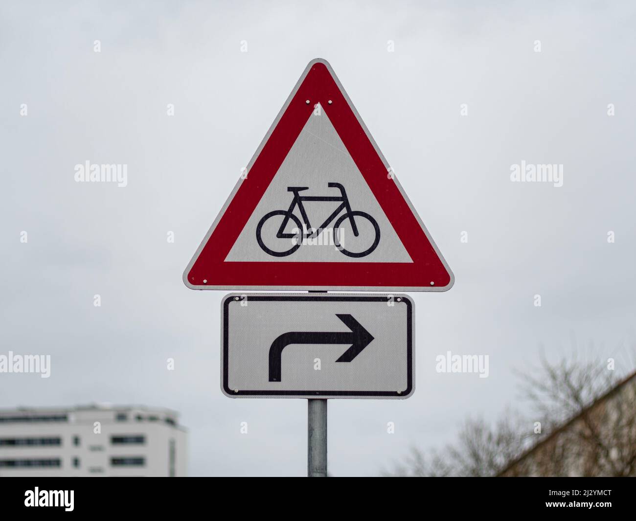 Segnaletica stradale di avvertimento per i ciclisti con una freccia a destra. Cartello stradale per prestare attenzione ai ciclisti in una città. Simbolo di fronte a un cielo coperto. Foto Stock