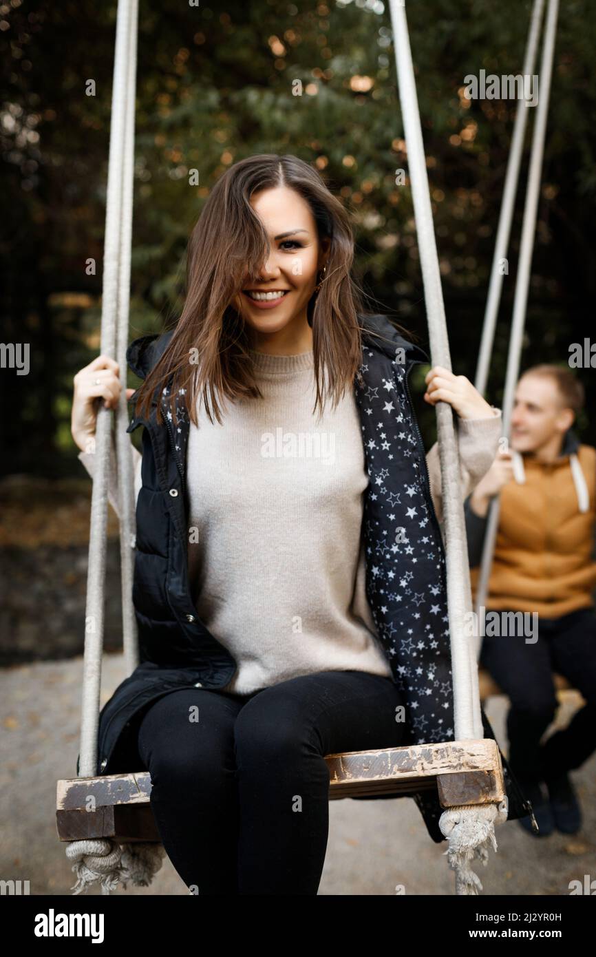 Felice giovane coppia di gara mista su una data oscillando su un altalena, in primo piano è una donna con capelli lisci e un sorriso bianco neve, sullo sfondo un giovane sorridente Foto Stock