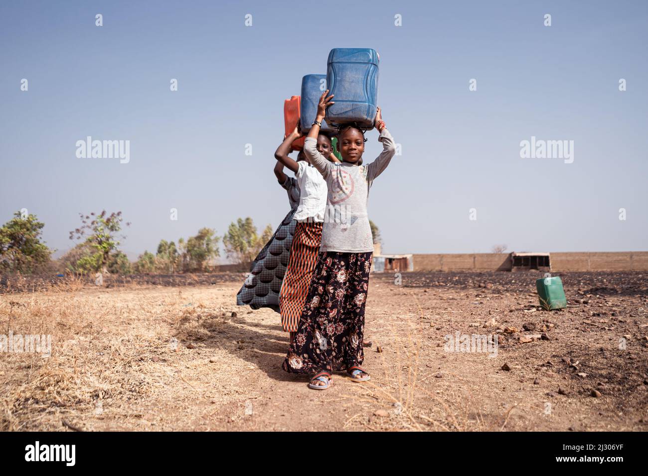 Piccola processione di ragazze nelle campagne rurali africane impegnate nel trasporto di acqua potabile dal pozzo lontano al loro villaggio Foto Stock