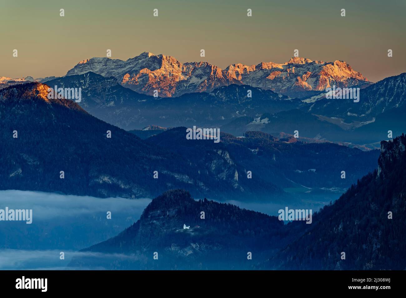 Atmosfera serale con nebbia a valle e vista di Petersberg con cappella, Madron e Loferer Steinberge, Montagne di Mangfall, Alpi bavaresi, alta Baviera, Baviera, Germania Foto Stock