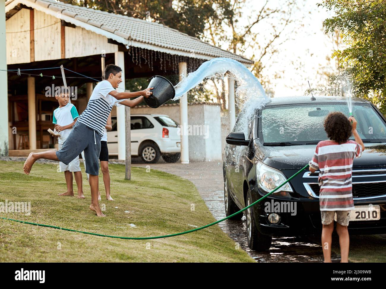 Guardate fuori ragazzi acqua in arrivo. Shot di un gruppo di bambini allegri che lavano i loro genitori auto insieme fuori durante il giorno. Foto Stock