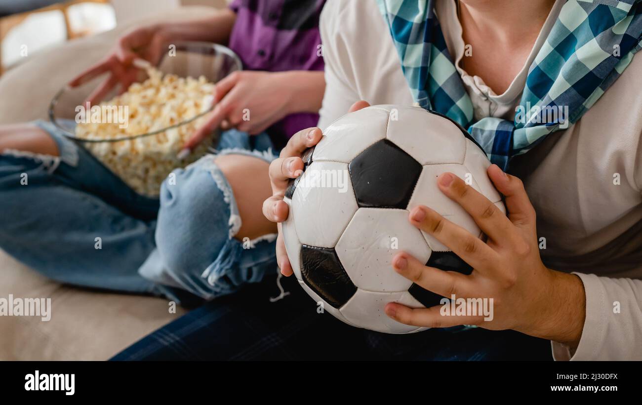 Primo piano sulle mani di un uomo caucasico sconosciuto che tiene la palla da calcio mentre guarda la partita a casa Foto Stock