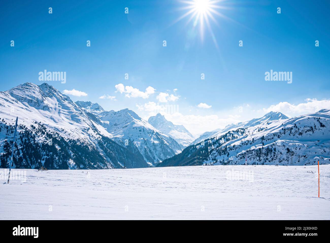 Vista panoramica del sole splendente attraverso il cielo blu sulle montagne innevate Foto Stock
