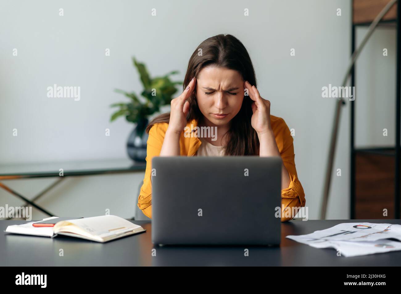 Caucasica giovane adulta donna d'affari, manager, freelancer o segretario che sperimenta stress al lavoro in ufficio, stanco di sedersi al lavoro su un computer portatile, massaggiando templi, occhi chiusi, ha bisogno di un riposo Foto Stock