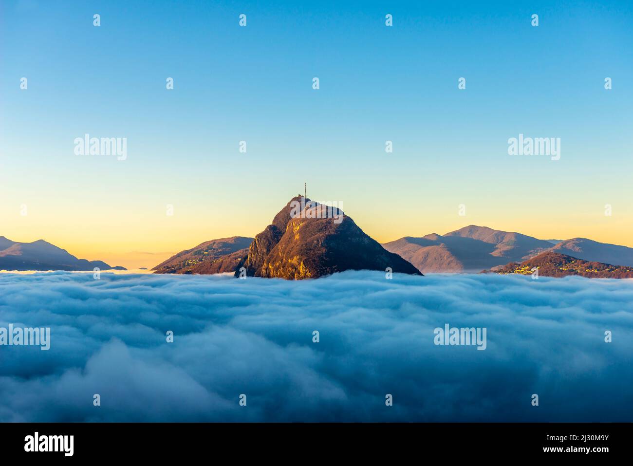 Picco di montagna San Salvatore al di sopra di Cloudscape con luce solare e cielo trasparente a Lugano, Ticino in Svizzera. Foto Stock