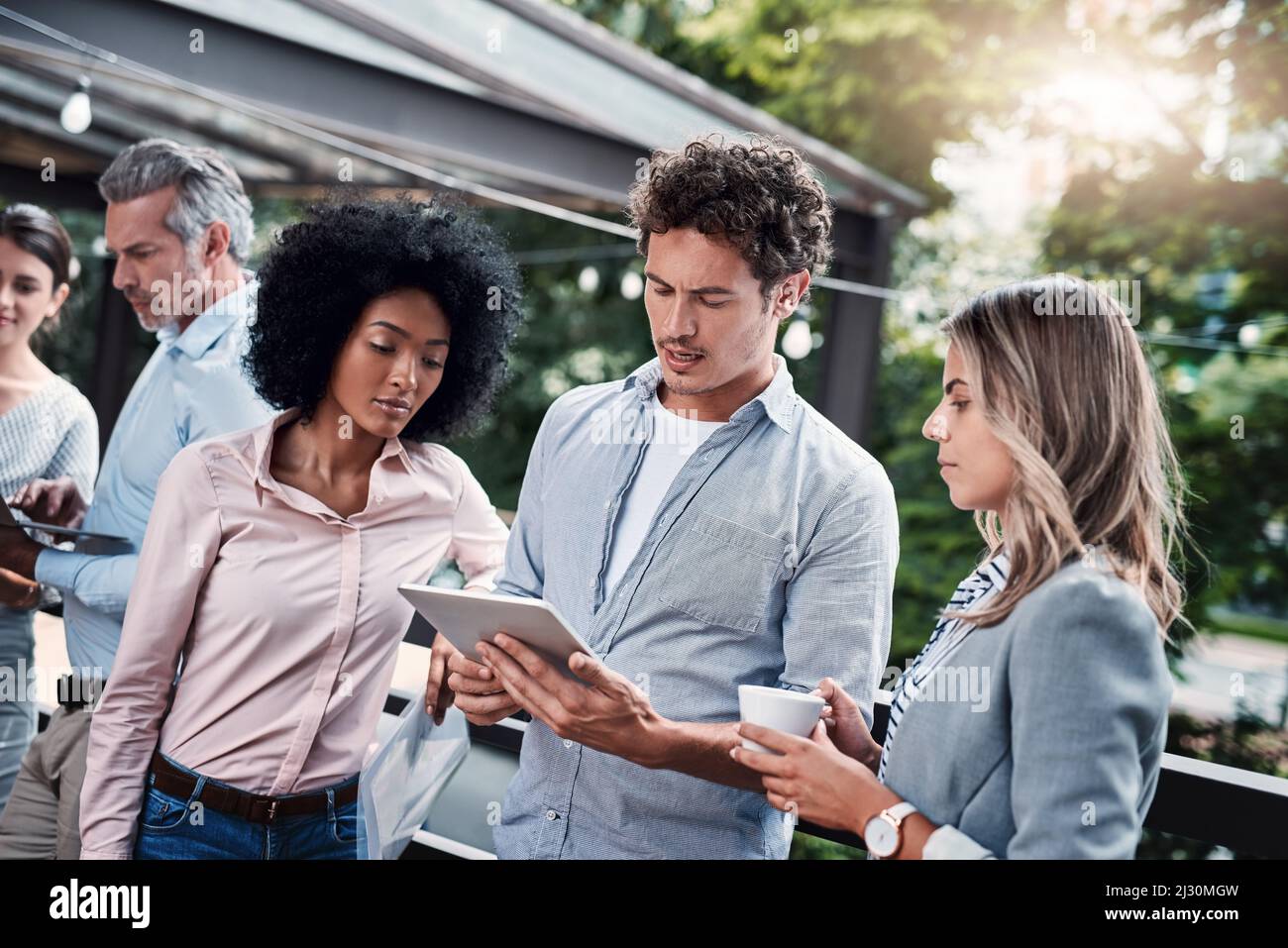 Lavorare come gruppo impegnato. Shot di un gruppo di uomini d'affari che lavorano insieme su un tablet digitale all'aperto. Foto Stock