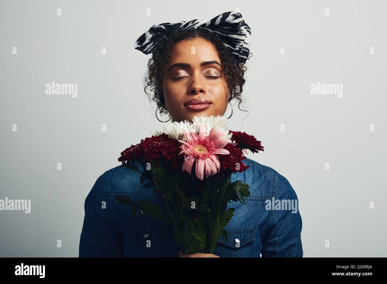 Il dolce odore di fiori mi calma. Studio girato di una giovane donna attraente che tiene un mazzo di fiori su uno sfondo grigio. Foto Stock