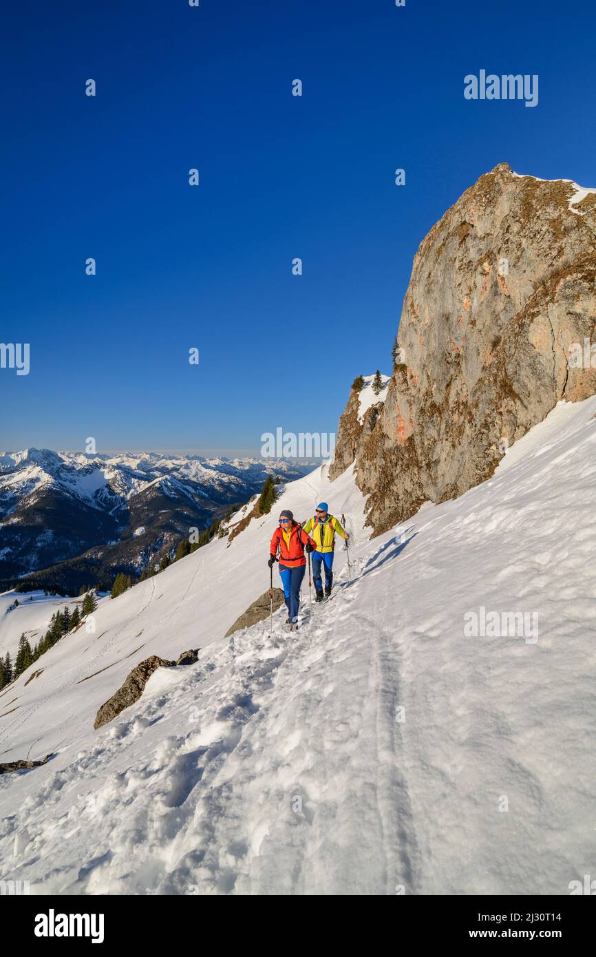 Uomo e donna che camminano fino al Rotwand attraverso il pendio di neve, torri di roccia sullo sfondo, Rotwand, Spitzing area, Alpi bavaresi, alta Baviera, Baviera, Germania Foto Stock