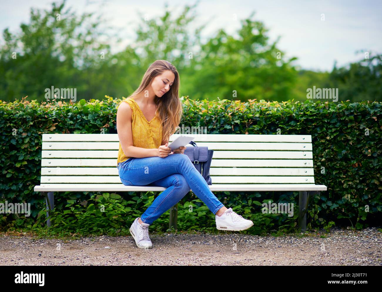 WIFI nel parcheggio e connettività. Scatto di una giovane donna utilizzando un tablet digitale su una panchina del parco. Foto Stock