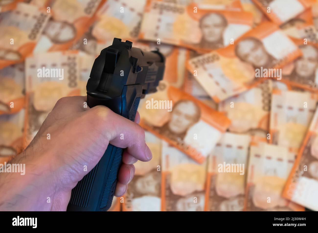 Tenendo una pistola e puntando verso uno sfondo di ventimila banconote cilene pesos. Foto Stock