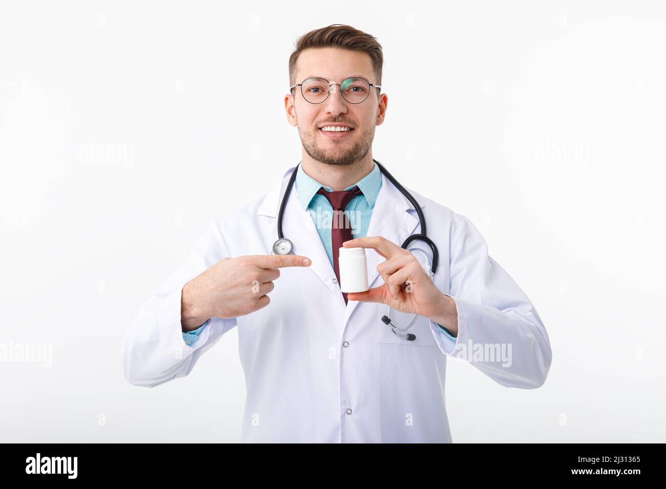 Un giovane e allegro medico maschio tiene in mano un medicinale e lo indica con un gesto. Foto Stock