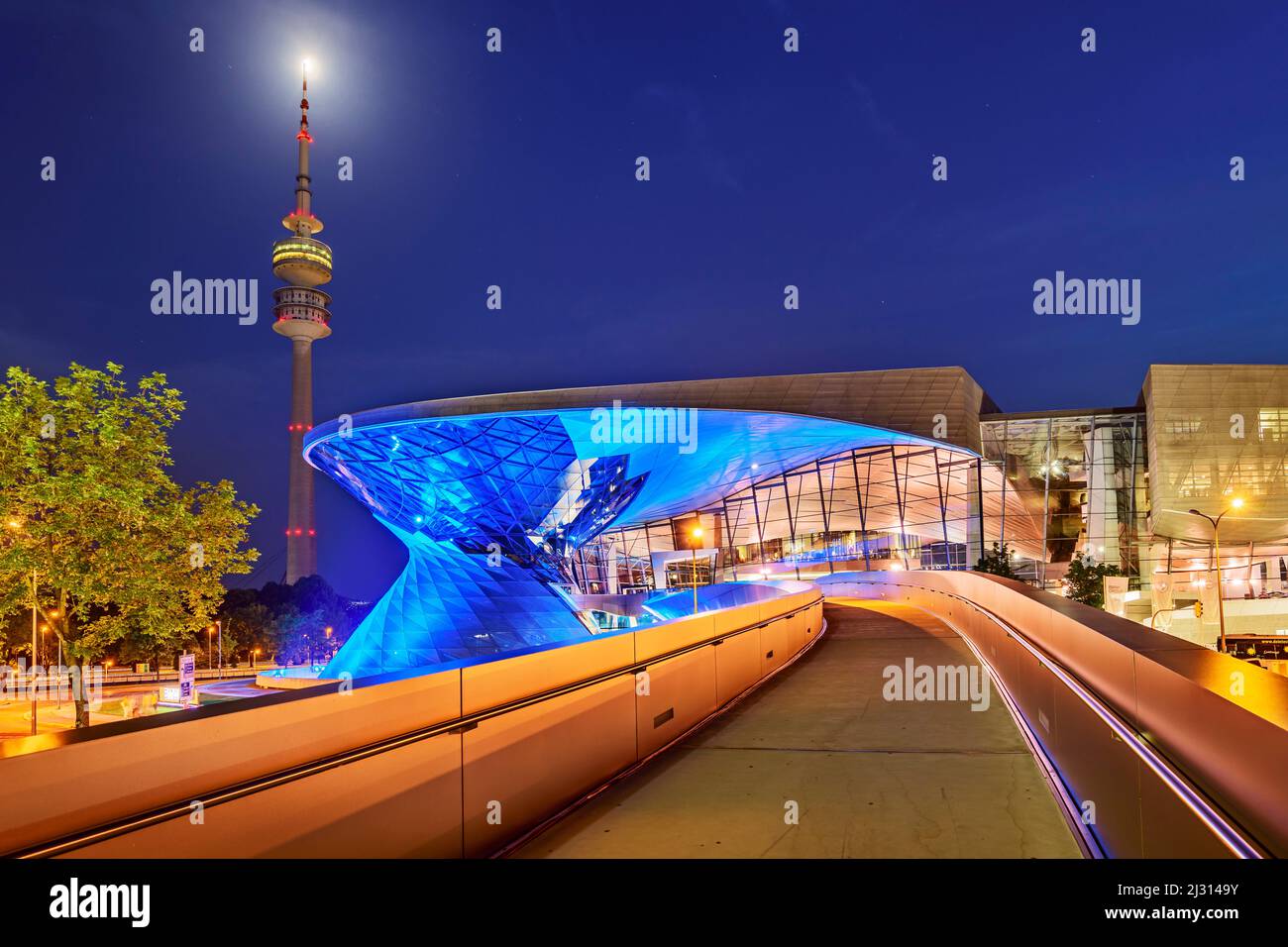 Edificio blu illuminato BMW Welt con la Torre Olimpica sullo sfondo, Monaco, Baviera alta, Baviera, Germania Foto Stock
