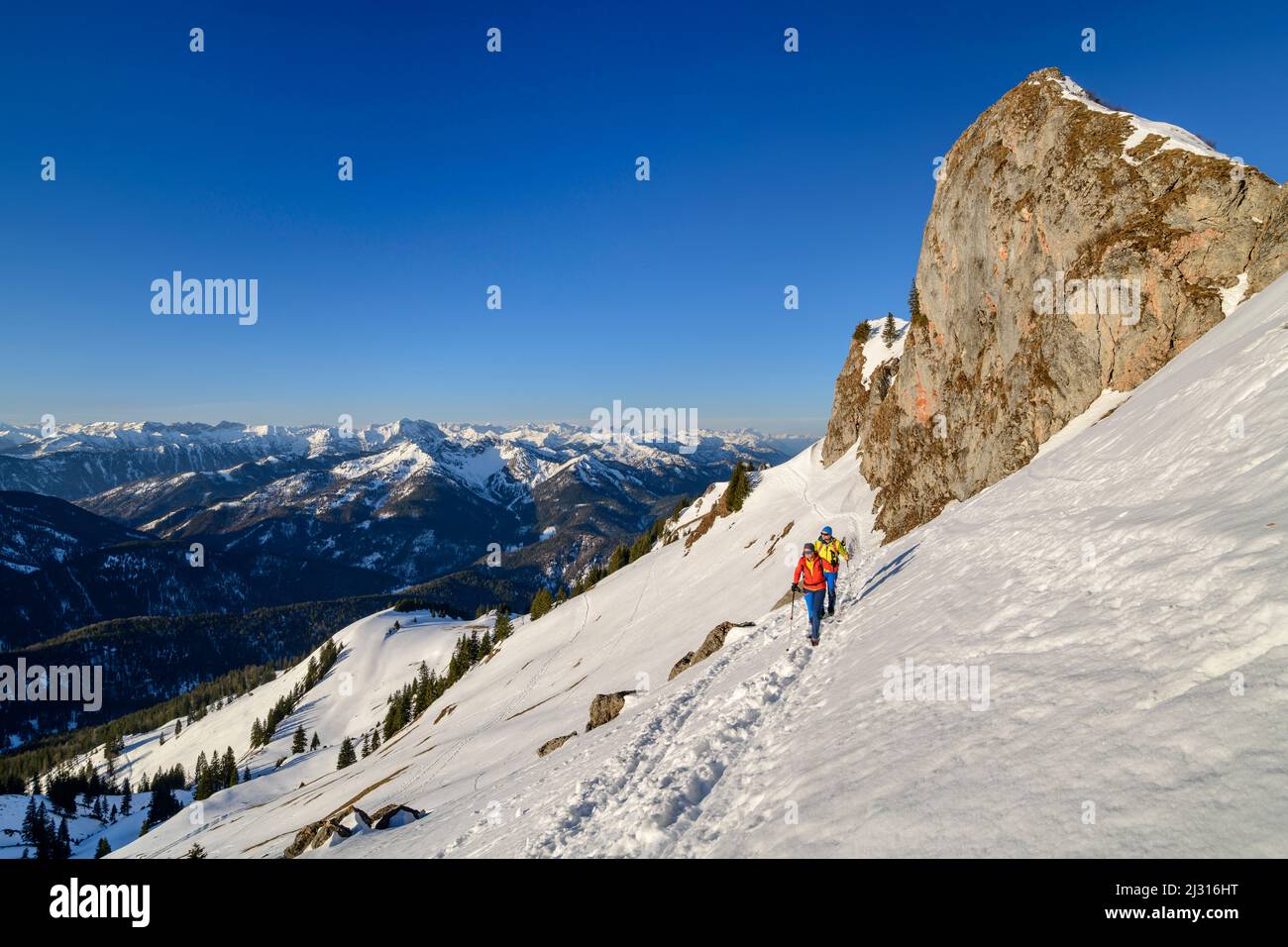 Uomo e donna che camminano fino al Rotwand attraverso il pendio di neve, torri di roccia sullo sfondo, Rotwand, Spitzing area, Alpi bavaresi, alta Baviera, Baviera, Germania Foto Stock