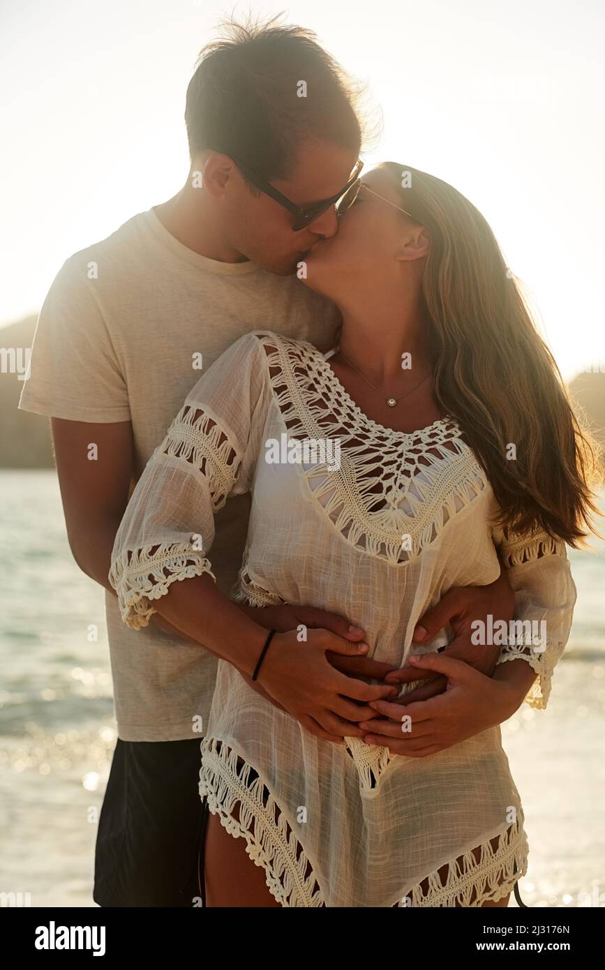 Baci in riva al mare. Scatto di una giovane coppia affettuosa sulla spiaggia al tramonto. Foto Stock