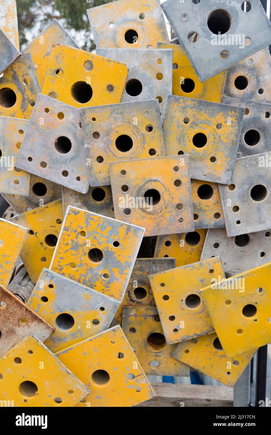 Un mucchio di piastre di base del martinetto per ponteggi forma un disegno colorato di acciaio, vernice gialla e buchi neri Foto Stock
