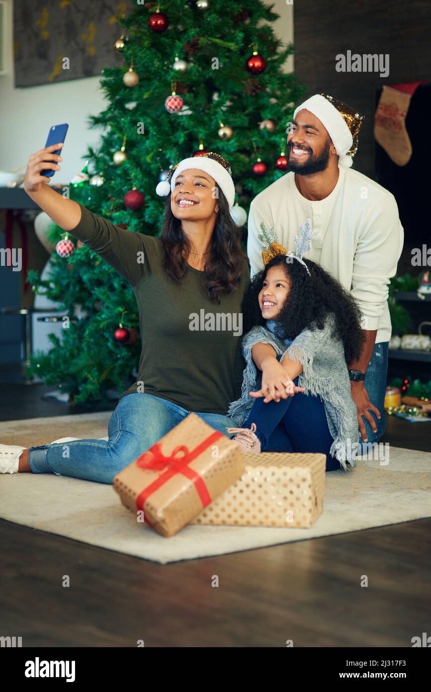 I ricordi della famiglia felici scaldano quei freddi giorni di dicembre. Scatto di una giovane famiglia felice che prende selfie mentre apre i regali di Natale a casa. Foto Stock