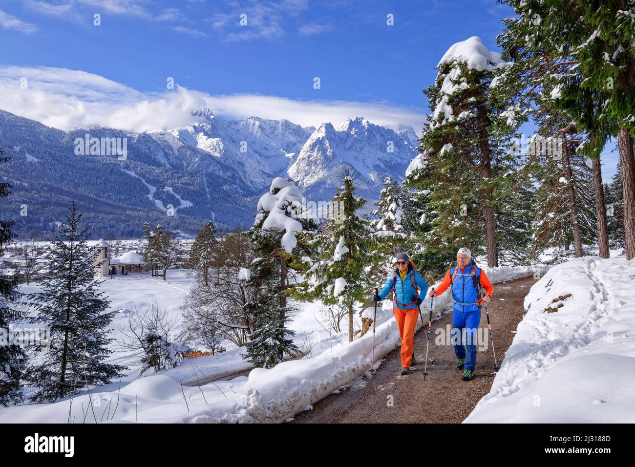 Escursioni uomo e donna su sentieri escursionistici sgomberati attraverso la foresta innevata, montagne Wetterstein sullo sfondo, Kramerplateauweg, Garmisch, Alpi Ammergau, Werdenfelser Land, Baviera superiore, Baviera, Germania Foto Stock