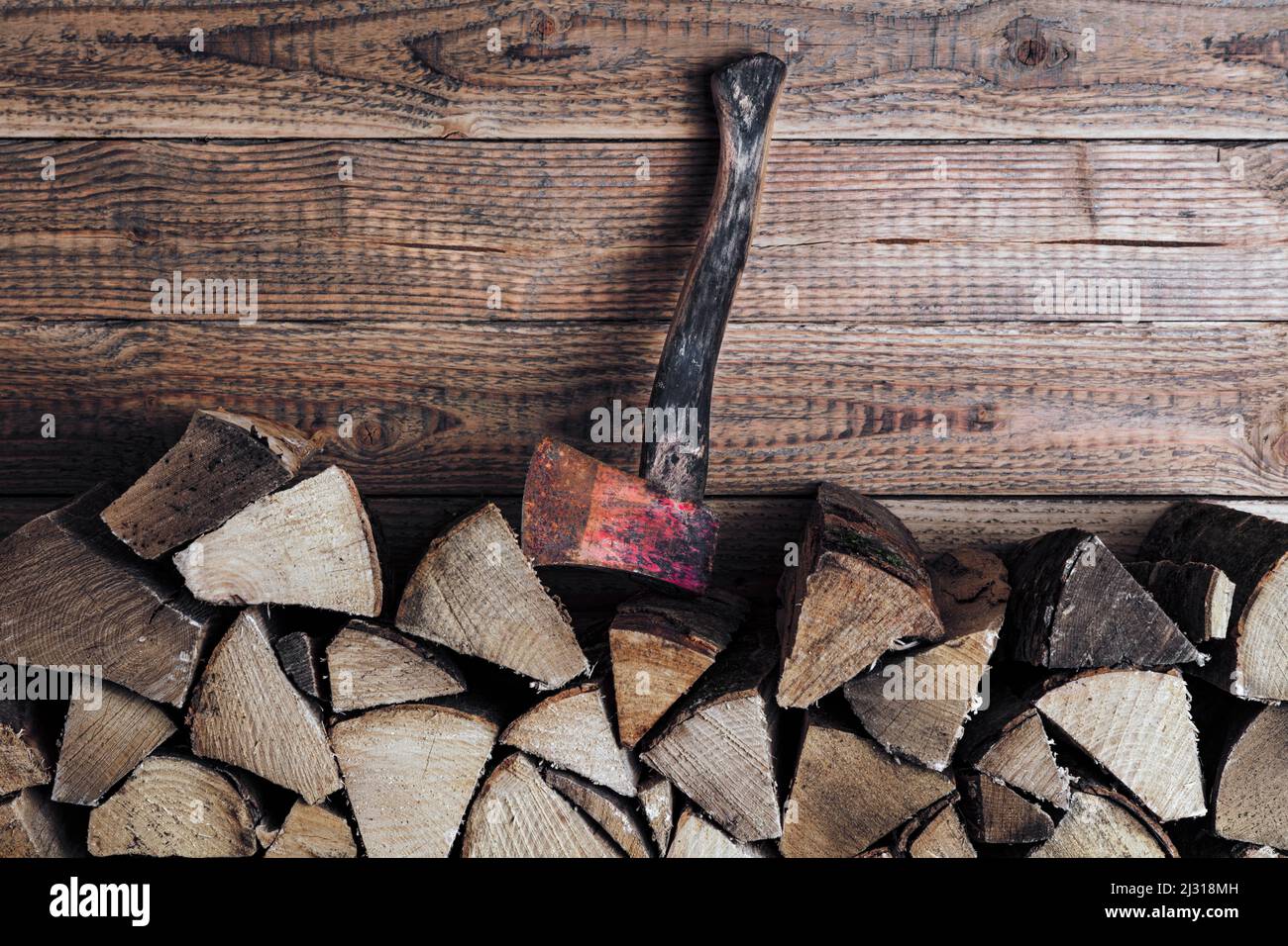 Brennholzstapel mit Axt vor Holzwand Foto Stock