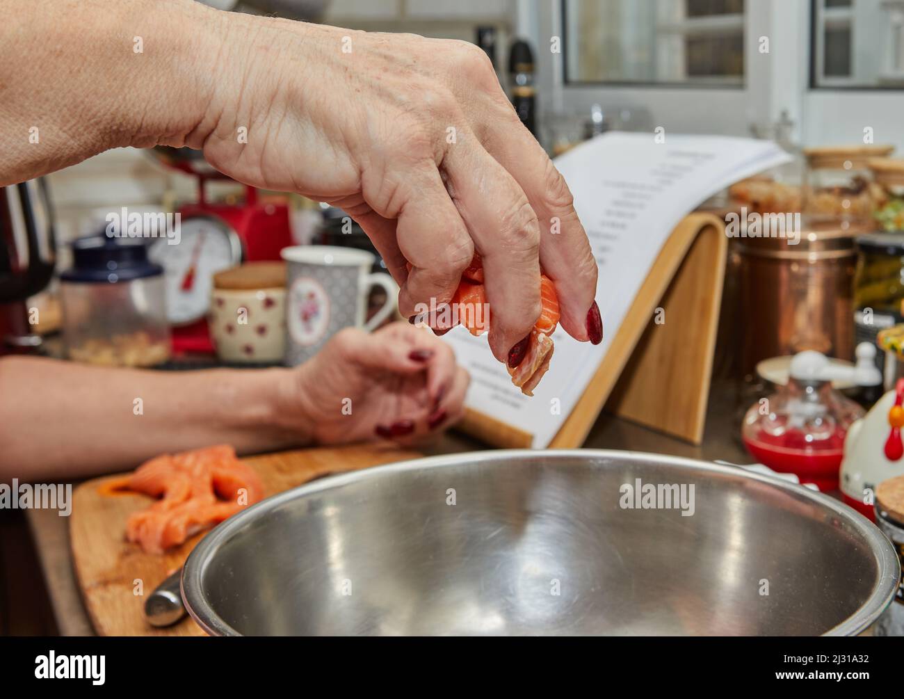 Lo chef lancia i cubetti di salmone in una ciotola per preparare la ricetta da internet Foto Stock