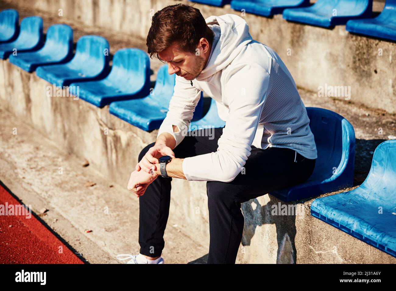 Uomo seduto al posto dello stadio e controllo orologio fitness dopo gli esercizi Foto Stock