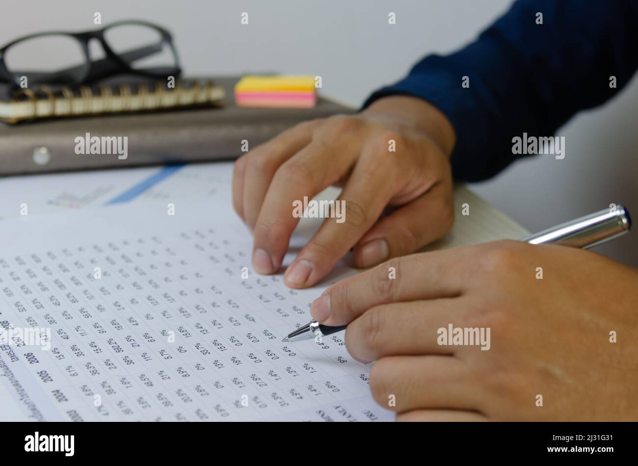 Mano dell'uomo che tiene una penna e carta del documento che commercializza i programmi finanziari di imposta ed investimento di affari. Foto Stock