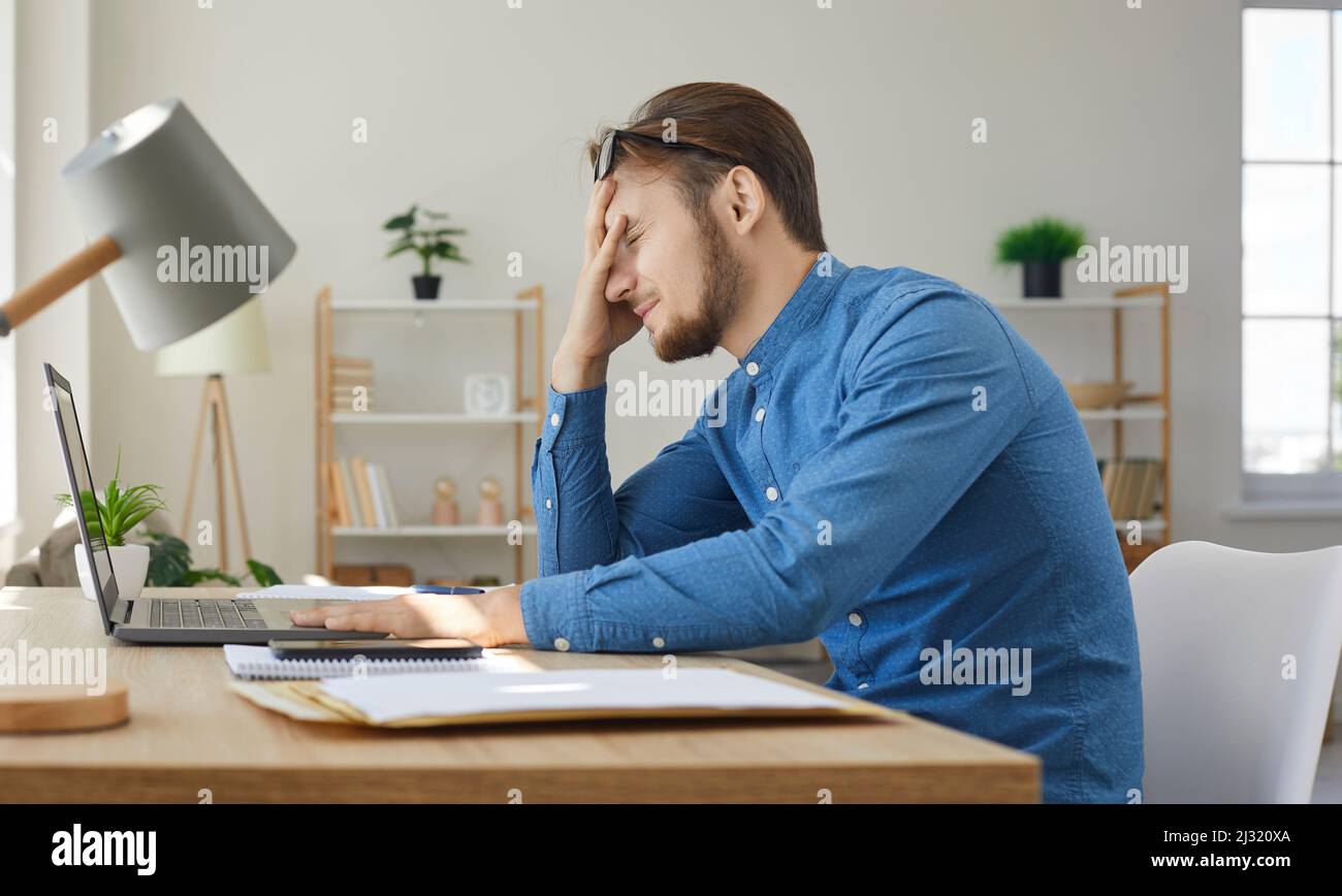 Stanco, stressato, frustrato giovane che ha avuto problemi mentre lavora sul suo laptop Foto Stock
