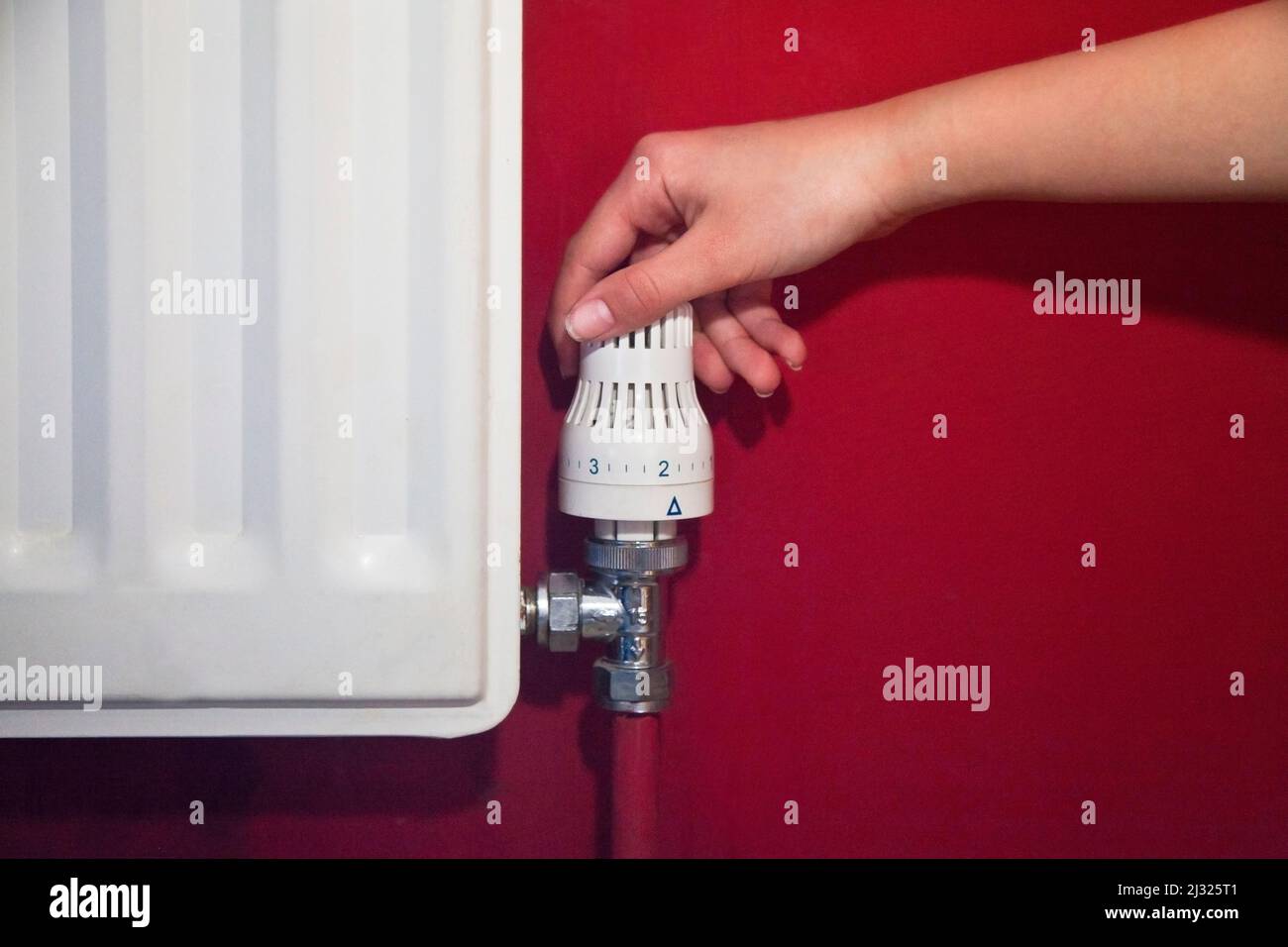 Una mano che abbassa la valvola di controllo del radiatore per risparmiare energia, su una parete rossa Foto Stock