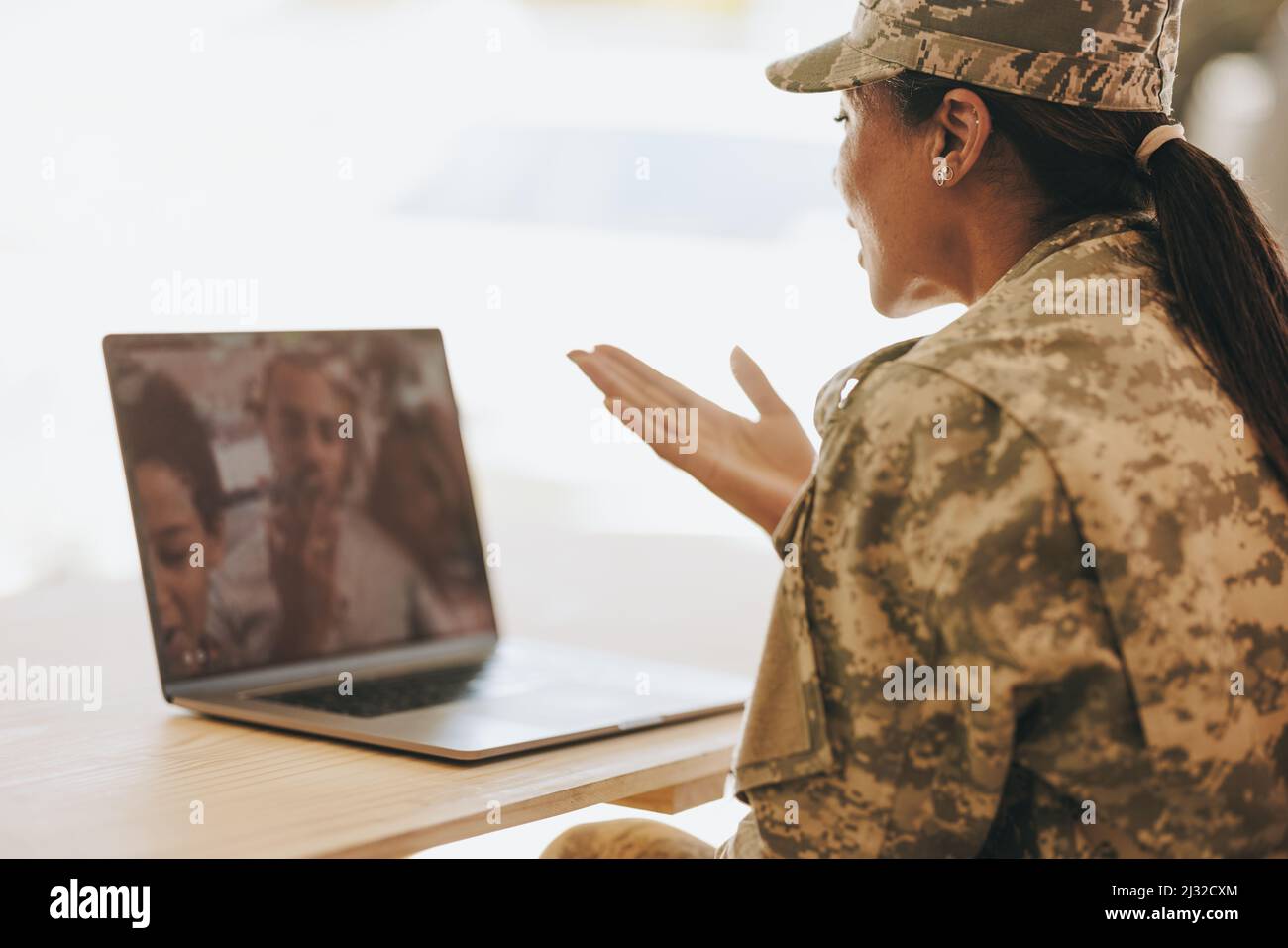 Una soldato femminile che soffia un bacio mentre videochiama suo marito e i suoi figli dalla base militare. Famiglia militare americana che comunica online. Foto Stock