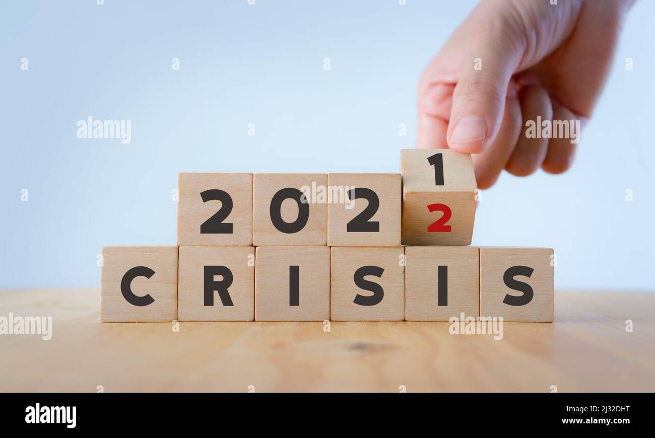 Concetto di gestione delle crisi nel nuovo anno 2022 . Effetti imprevisti sulla situazione aziendale e sulla vita. La mano ribalta i cubi di legno da 2021 a 2022 con il testo 'CRISI Foto Stock
