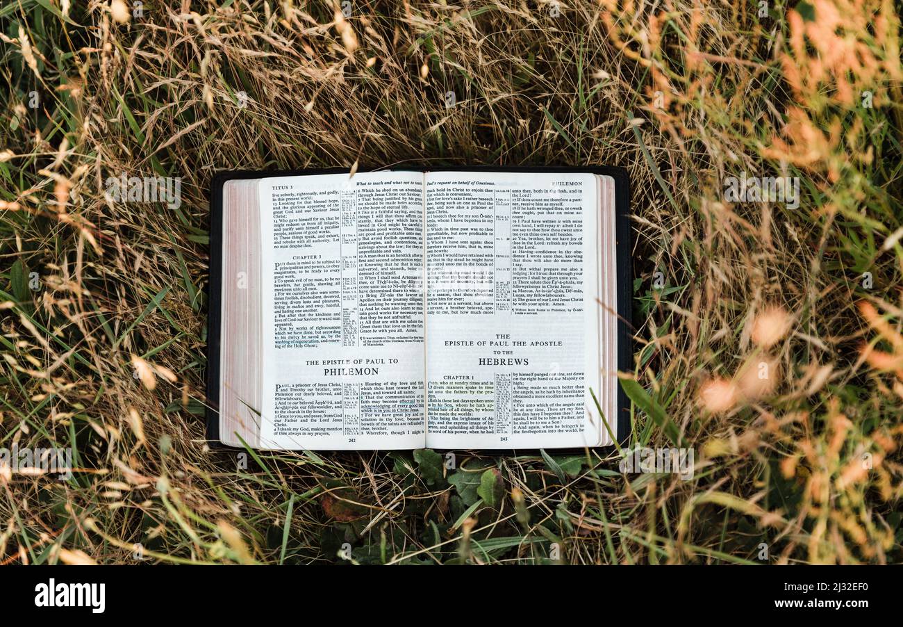 La Sacra Bibbia cristiana si apre in un campo caldo e soleggiato alle nuove lettere testamentari dei libri di Paolo di Filemone ed Ebrei Foto Stock