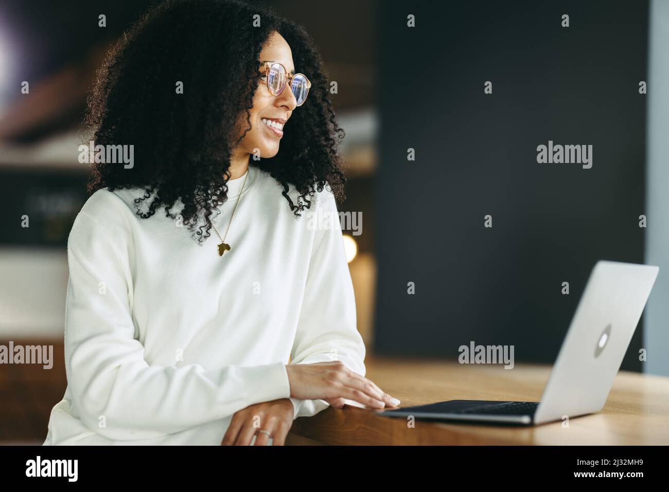 Giovane donna d'affari allegra che guarda via con attenzione mentre lavora con un notebook. Felice etnia d'affari che lavora a distanza in una moderna co-working Foto Stock