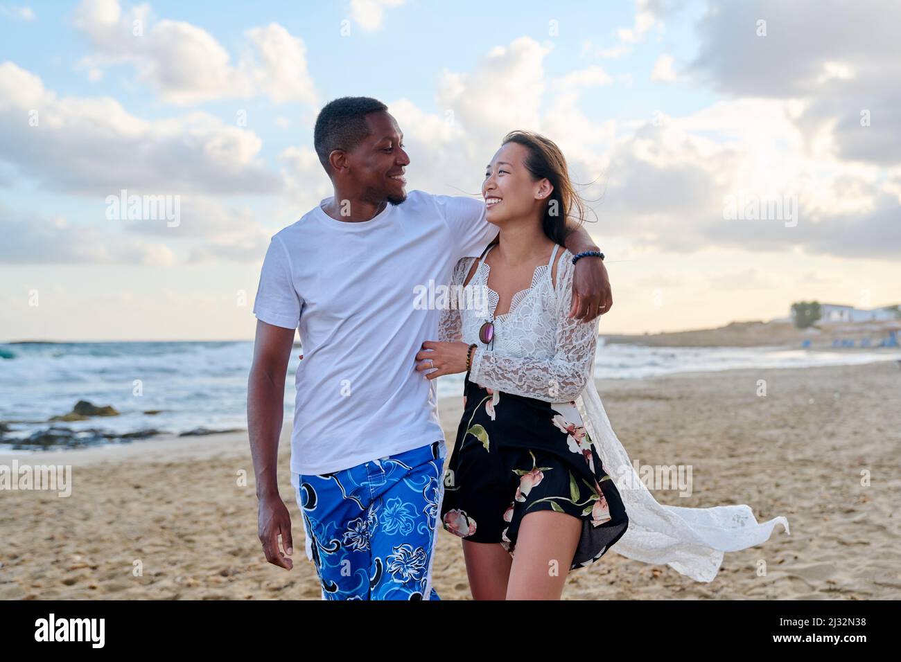 Giovane coppia felice che cammina sulla spiaggia tenendo le mani. Foto Stock