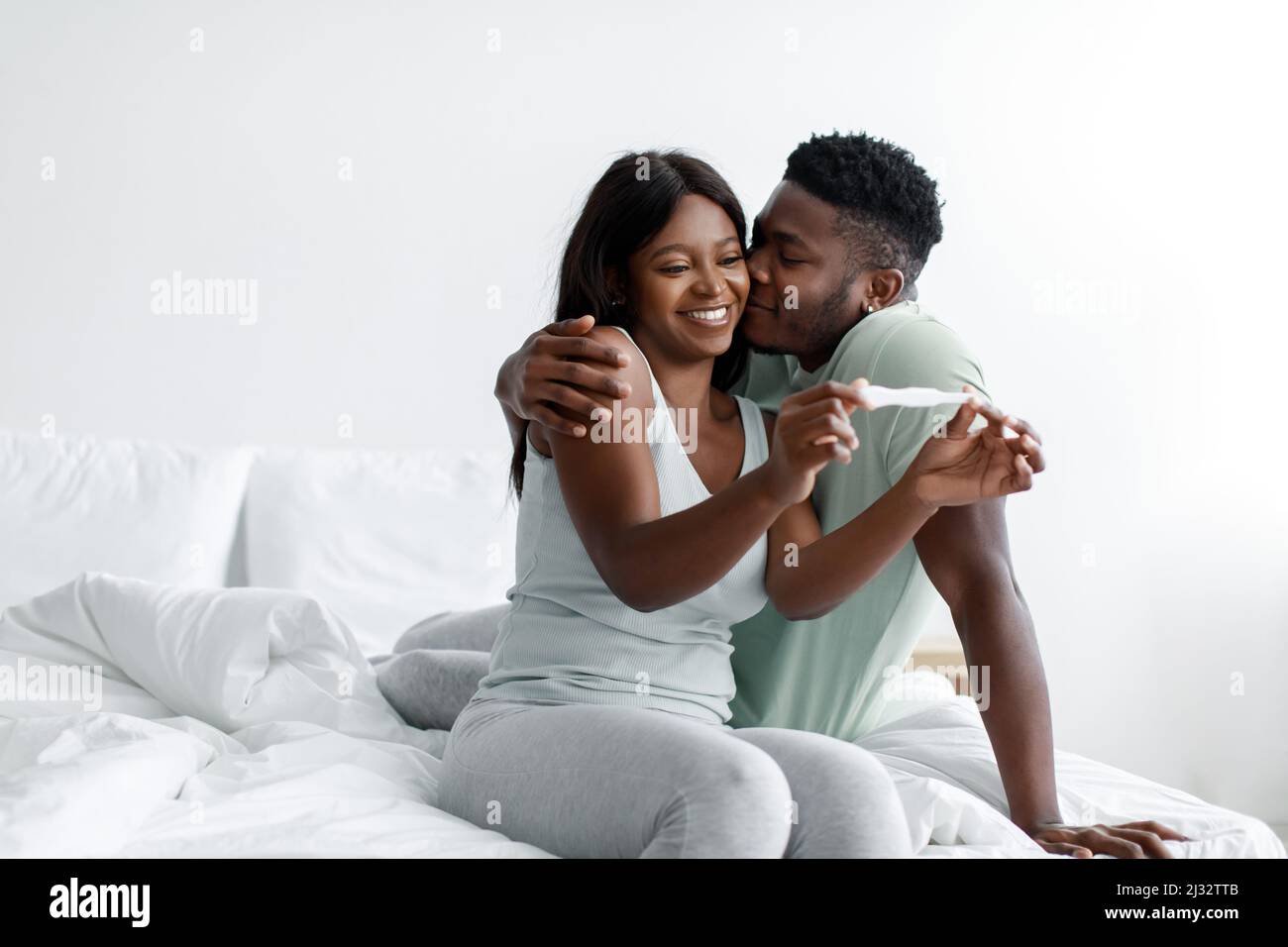 Felice felice millenario africano americano marito baciare moglie, coppia festeggiando il risultato positivo della gravidanza test Foto Stock