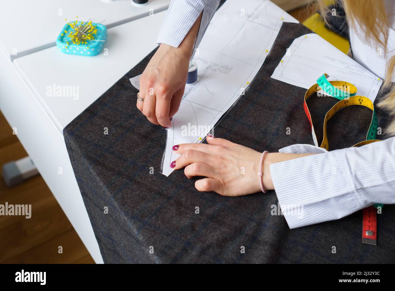 Il dressmaker contrassegna un pezzo di tessuto con gesso in base al modello di carta. Lavoro di sarto, utensili per cucire Foto Stock