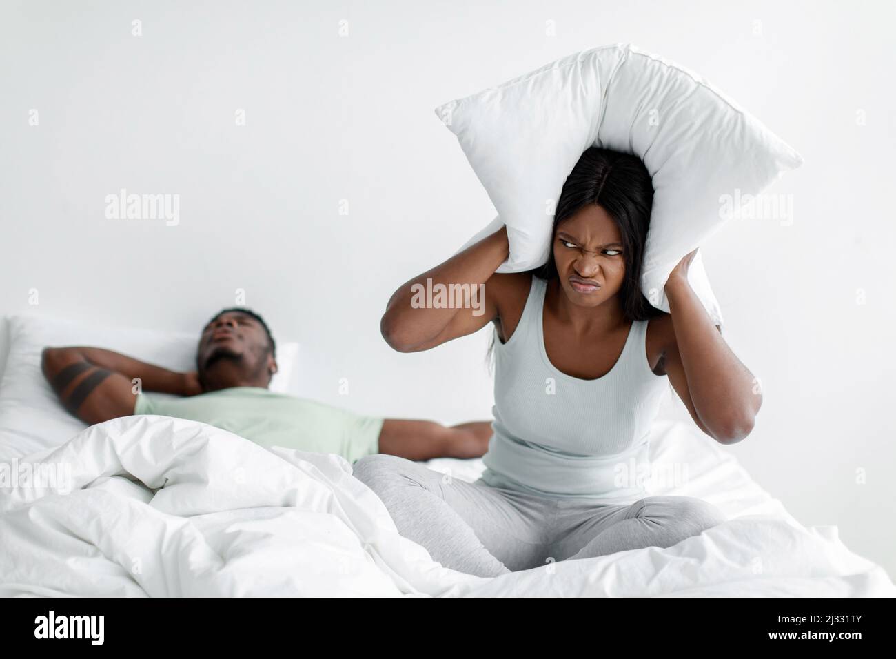 Disperata triste millennial african american signora freaking fuori, si siede sul letto e coprendo le orecchie con cuscino Foto Stock