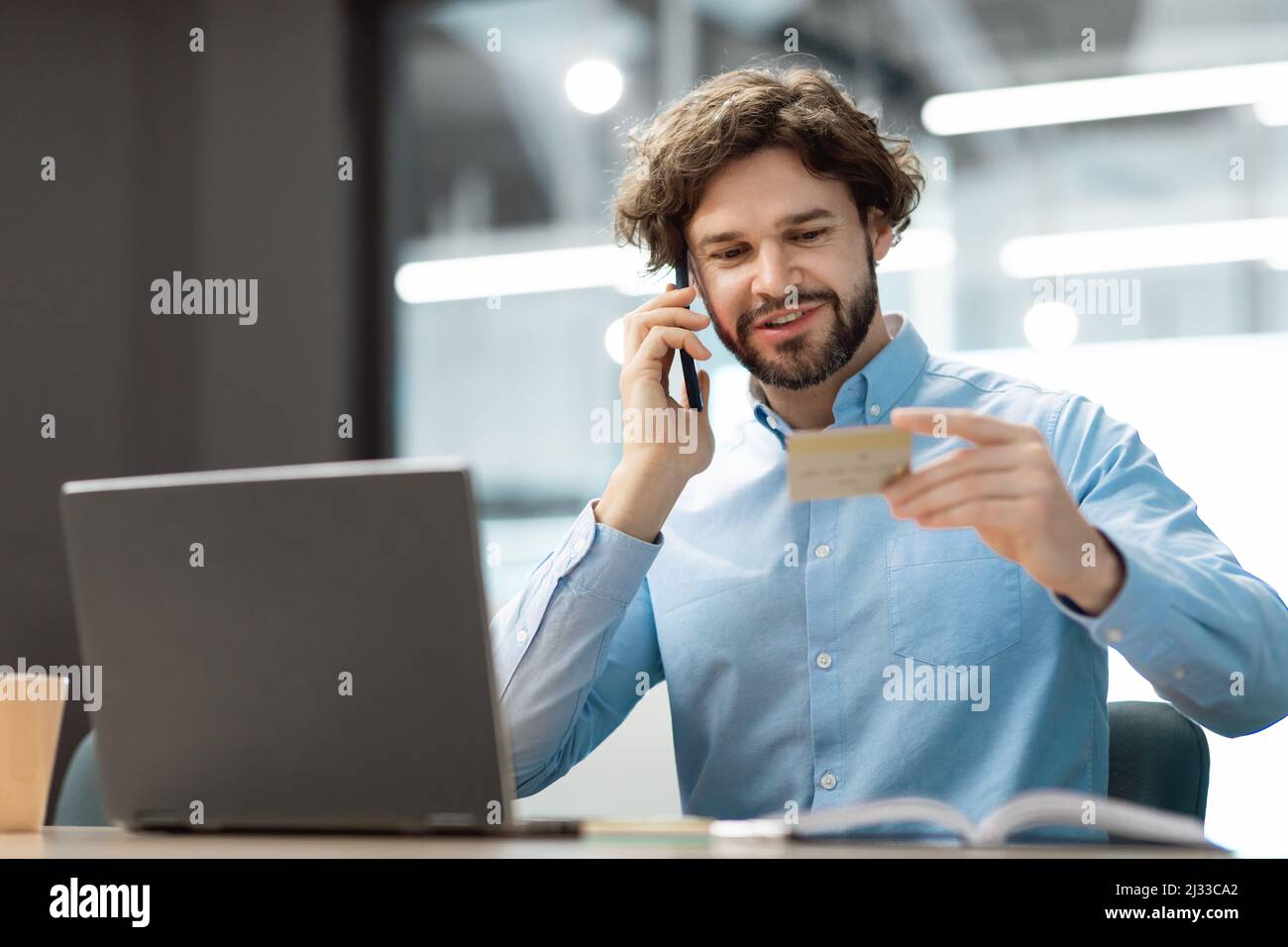 Uomo sorridente che usa la carta di credito che parla sullo smartphone Foto Stock