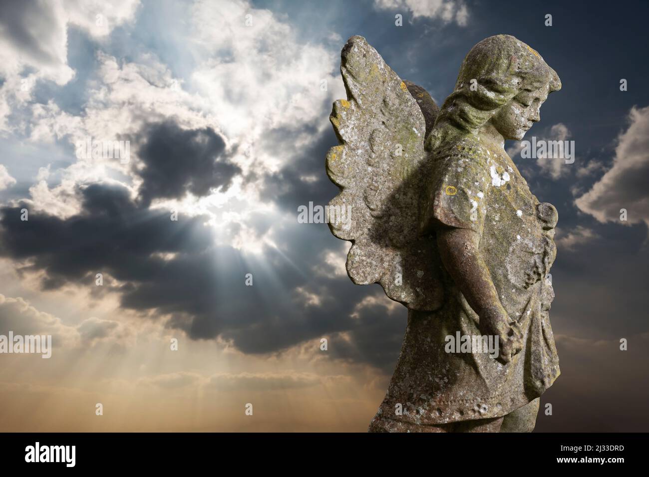 Statua di pietra di angelo alato contro i raggi di luce del sole dietro le nuvole Foto Stock
