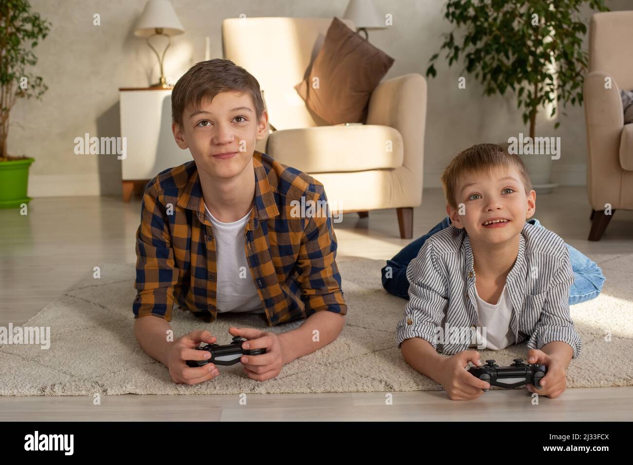 Due ragazzi gioiosi si trovano sul pavimento in una stanza che gioca con i videogiochi con i joystick Foto Stock