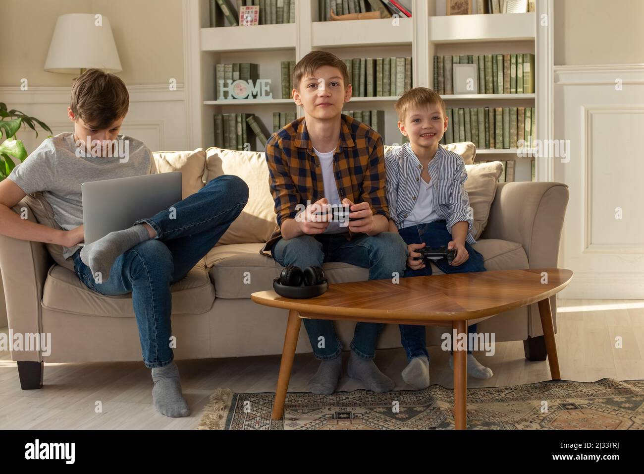 Tre fratelli ragazzi che giocano a videogame su un computer portatile e videogiochi con joystick nelle loro mani Foto Stock