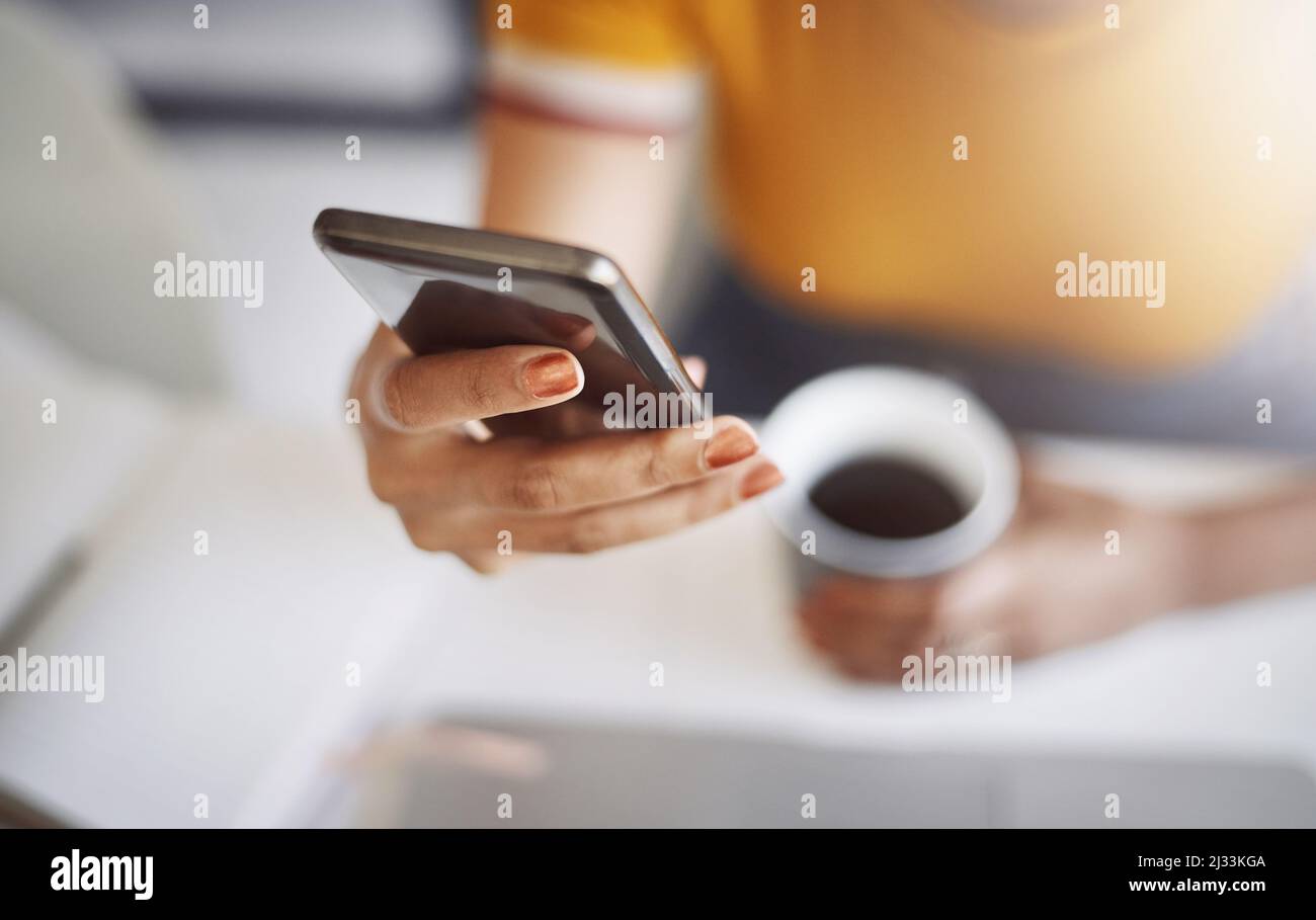 Shes ha ottenuto il suo cellulare e caffè, pronto per la giornata. Primo piano di un'irriconoscibile designer femminile utilizzando un cellulare nel suo ufficio domestico. Foto Stock