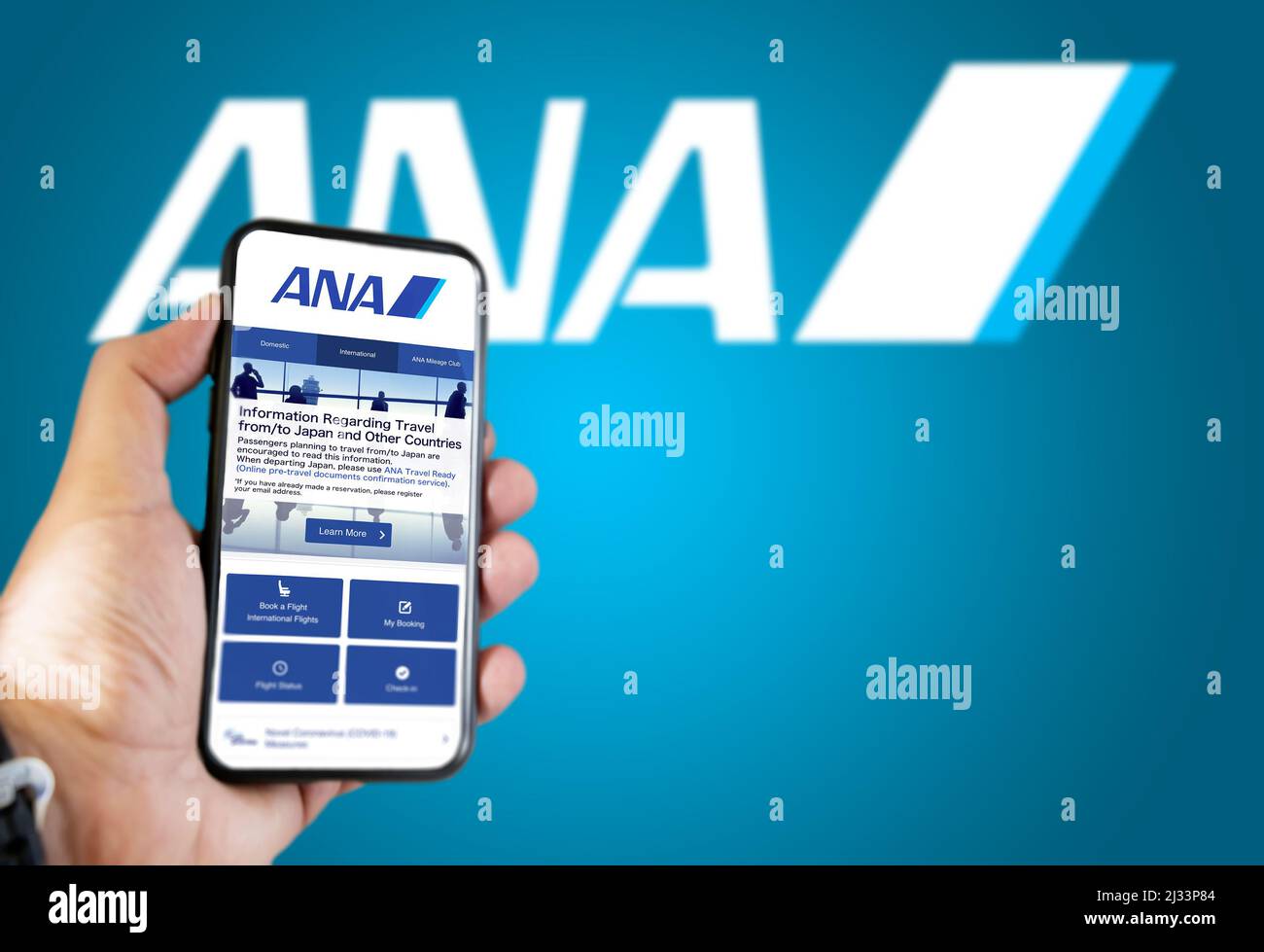 Tokyo, JAP, gennaio 2022: Tenere un telefono con ANA All Nippon Airways richiesta di prenotazione volo. Logo Ana sfocato su sfondo blu. Prenotazione Foto Stock