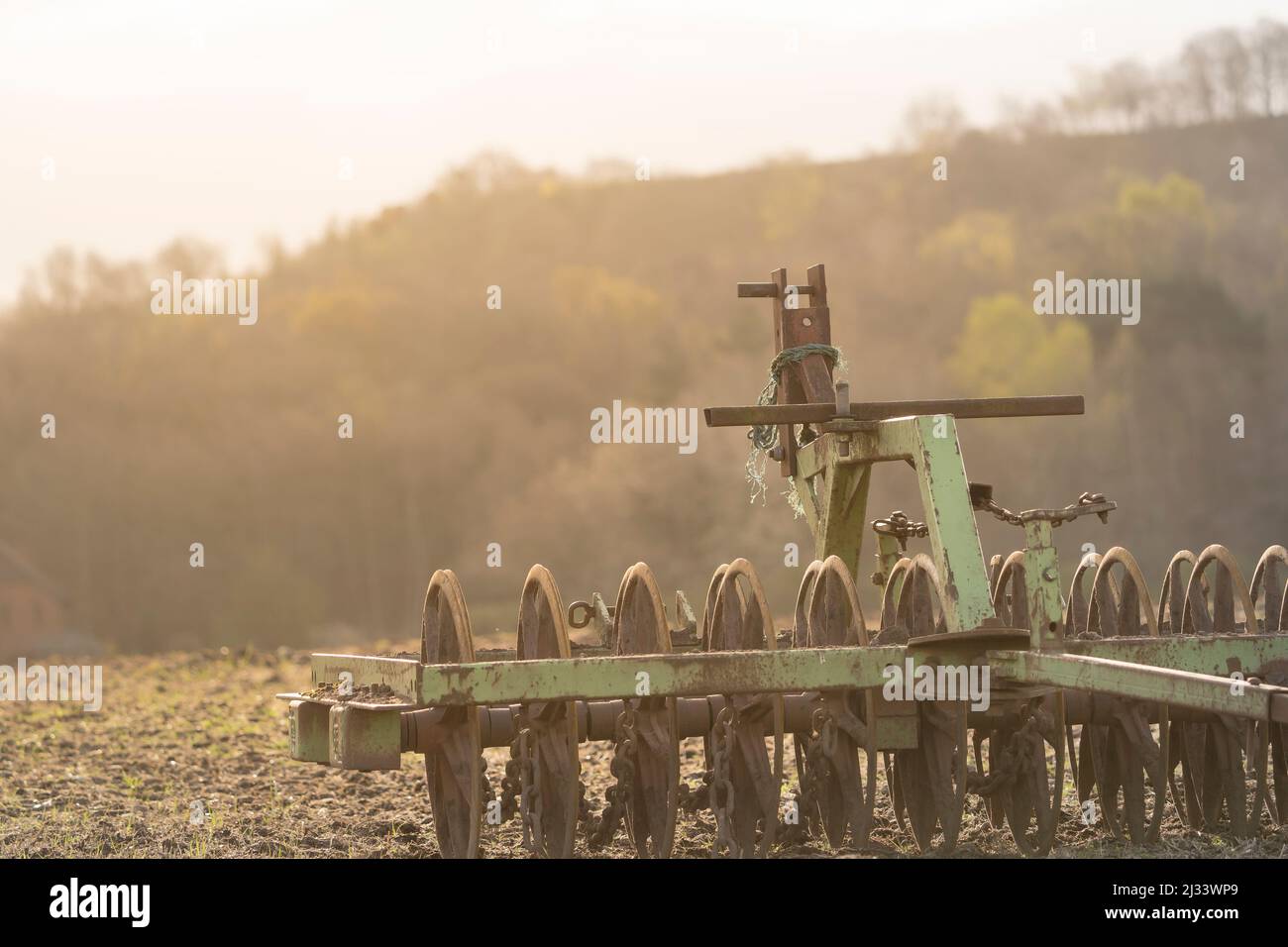 Un rastrello meccanico a terra degli agricoltori in un campo retroilluminato con sole al mattino presto Foto Stock