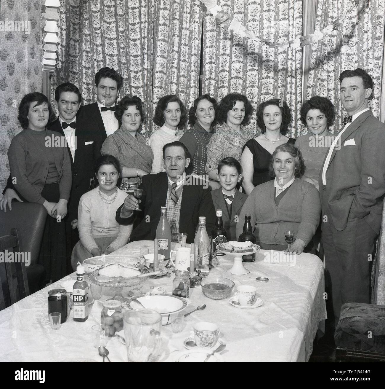 1961, storico, festa di famiglia, vestito per l'occasione, uomini e donne  si siedono e si levano in piedi intorno al tavolo del pasto per una foto di  gruppo, Stockport, Manchester, Inghilterra, Regno