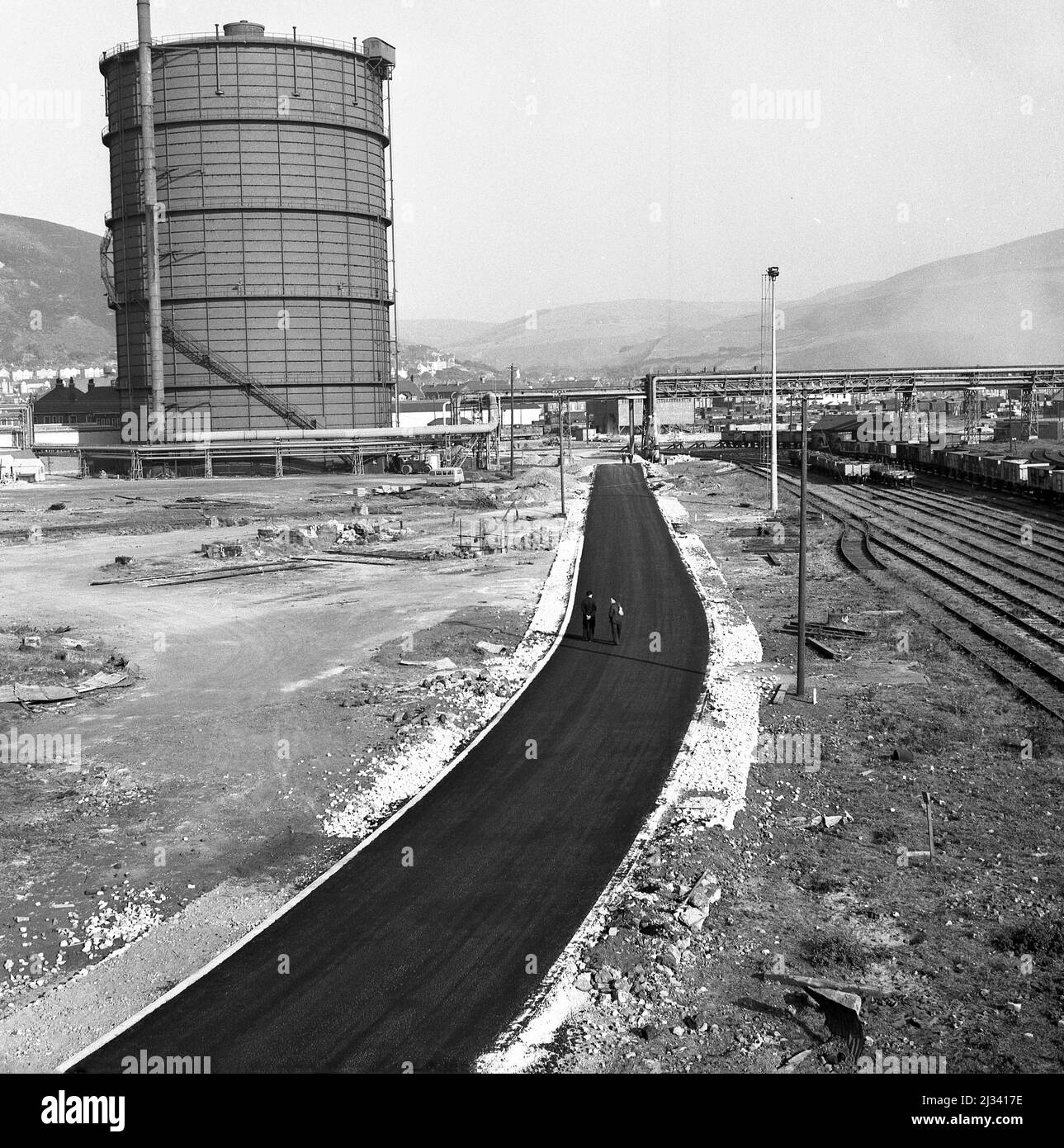 1950, storico, il gigantesco stabilimento di acciaio Abbey Works in costruzione, l'immagine mostra una strada di accesso alla fabbrica appena costruita accanto alle piste ferroviarie, Port Talbot, Galles, Regno Unito. Foto Stock