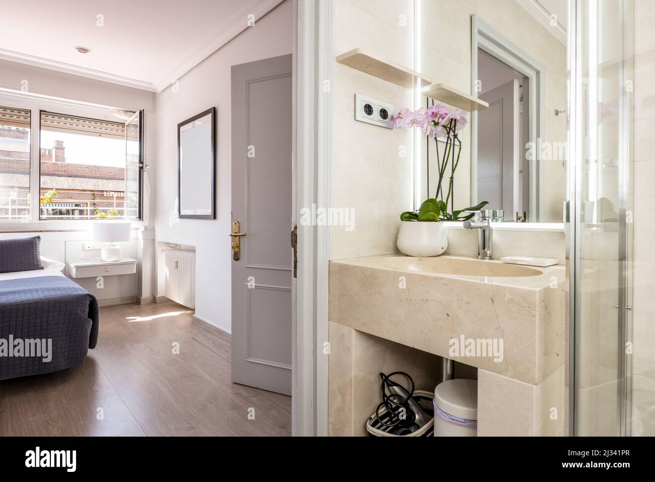 Bagno con lavandino in marmo color crema con specchio senza cornice e  accesso ad una camera da letto con grande finestra Foto stock - Alamy