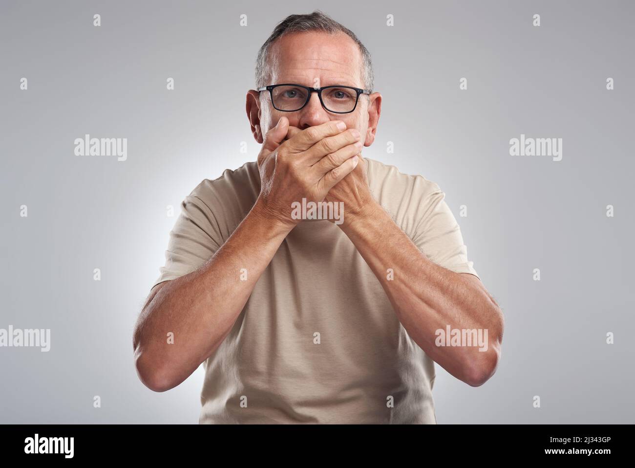 Non avrei dovuto dirlo. Scatto di un uomo maturo in piedi su uno sfondo grigio nello studio e coprendo la bocca con le mani. Foto Stock