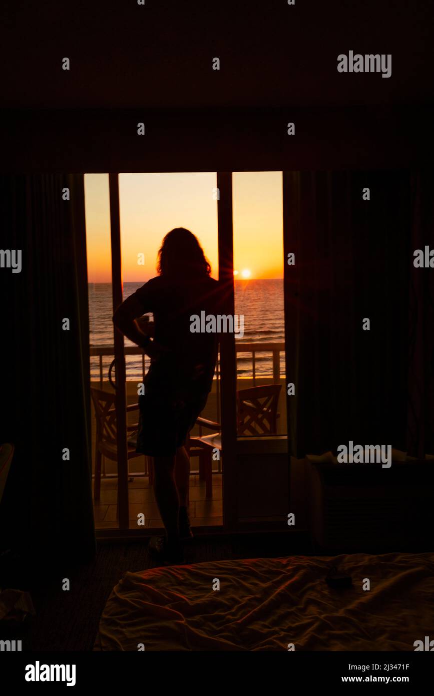 Silhouette di una persona, un uomo, in piedi su un balcone esterno che guarda l'alba sopra l'Oceano Atlantico. La persona è retroilluminata al mattino presto Foto Stock