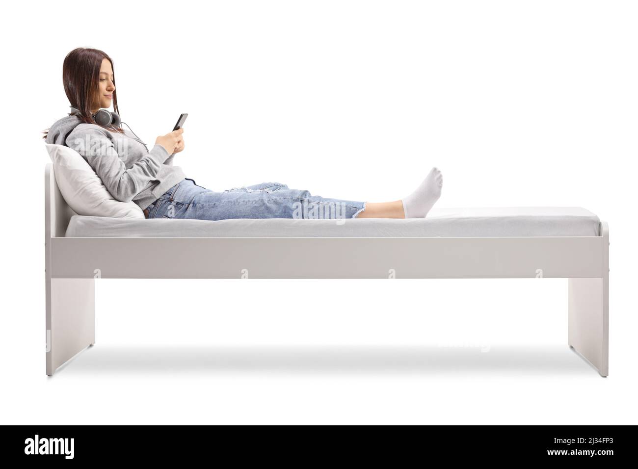 Adolescente femminile sdraiato su un letto e utilizzando uno smartphone isolato su sfondo bianco Foto Stock